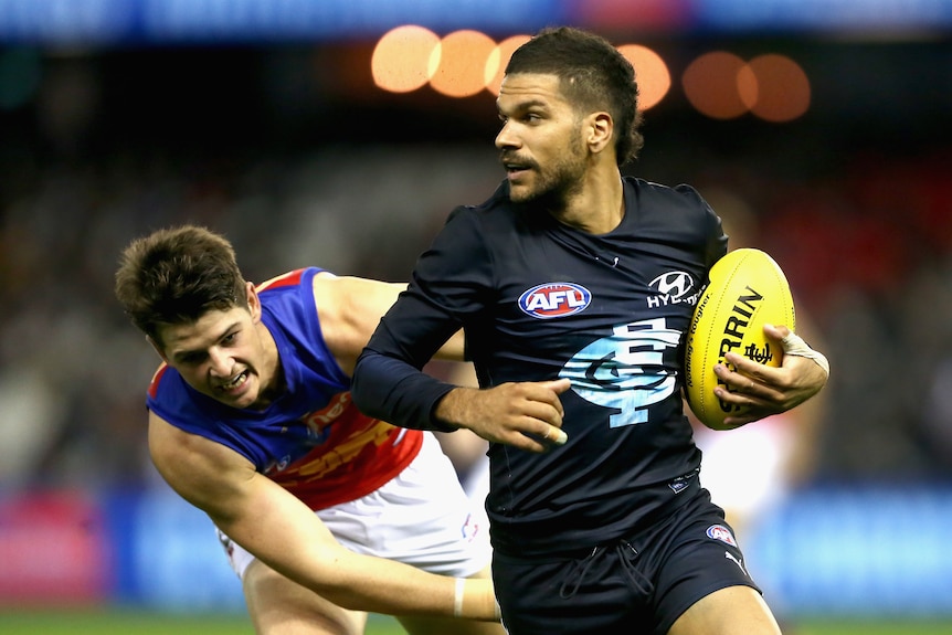 An AFL player leads the ball with a defender chasing him