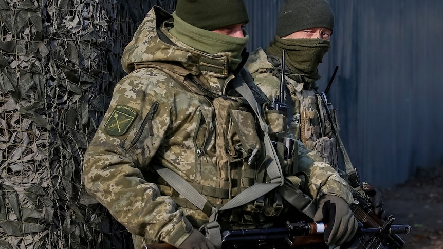 two soldiers in camouflage uniform and face scarfs stand next to each other