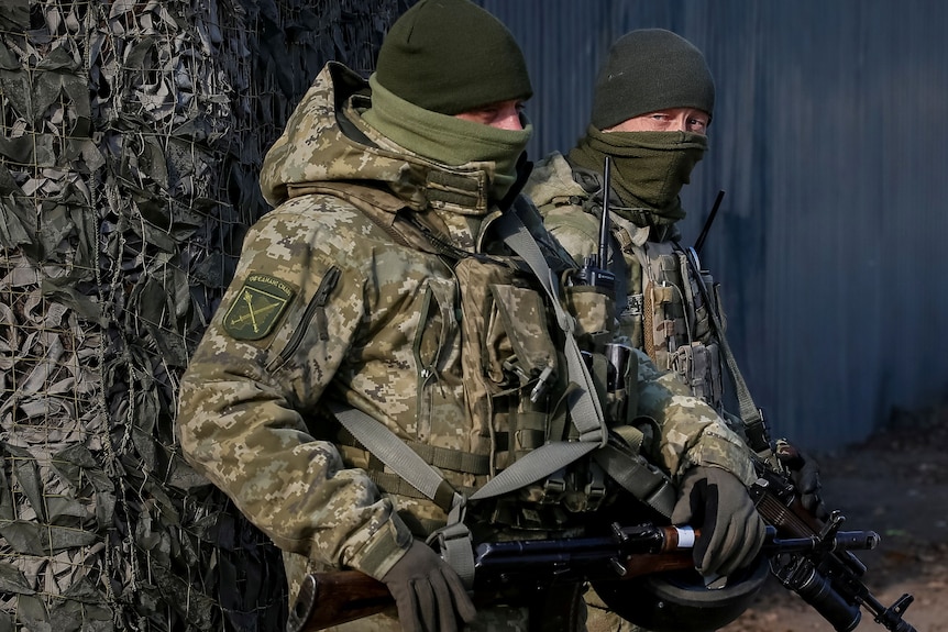 two soldiers in camouflage uniform and face scarfs stand next to each other