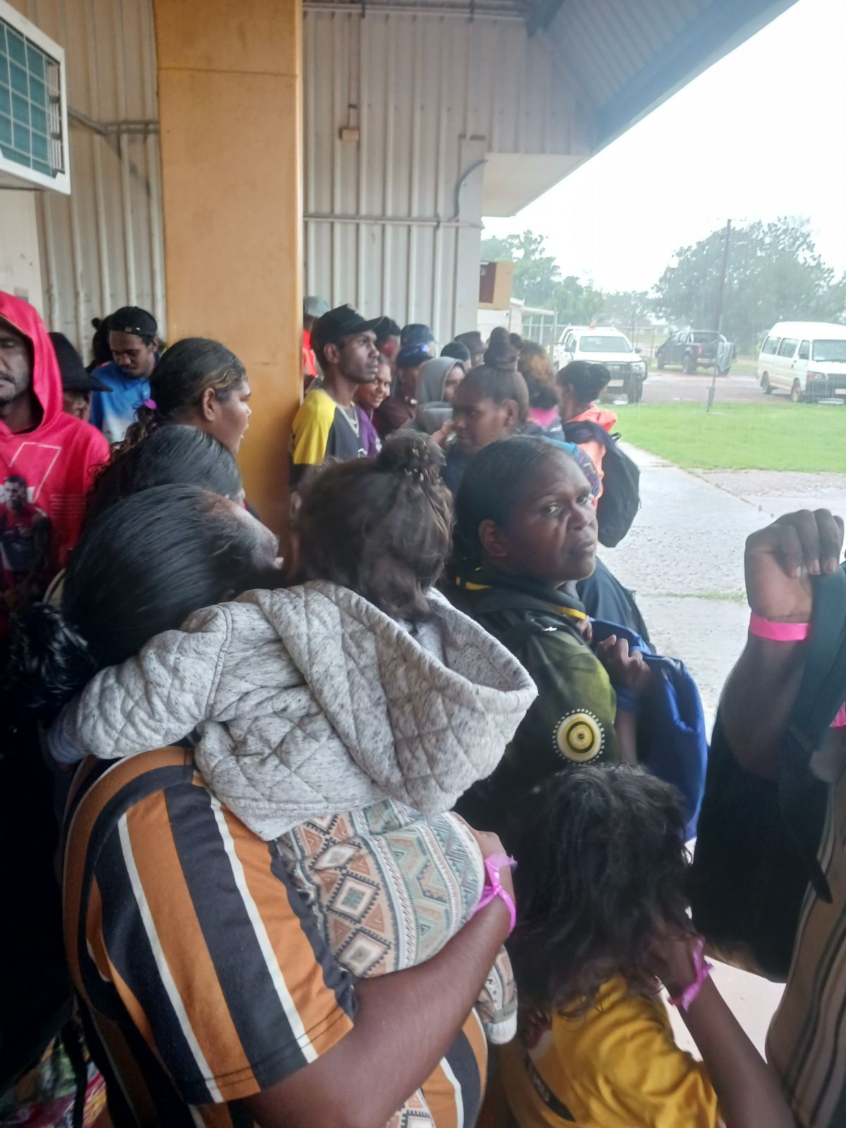 A group of people gathered under a tin building looking concerned.