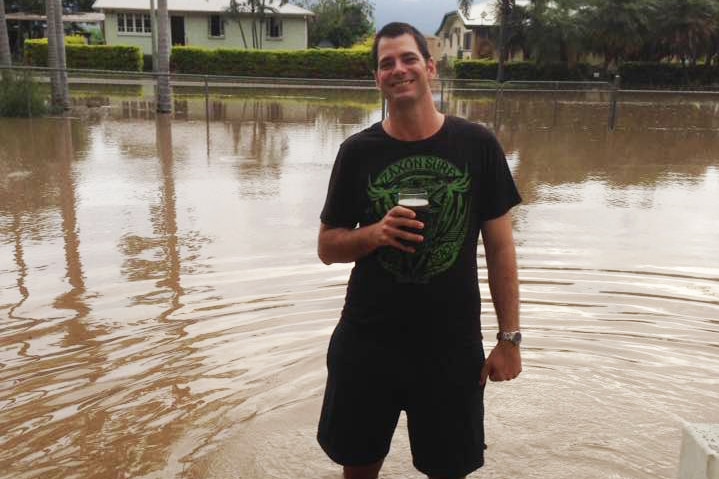 Giru resident Richard Berryman stands holding a beer in floodwaters outside his house.