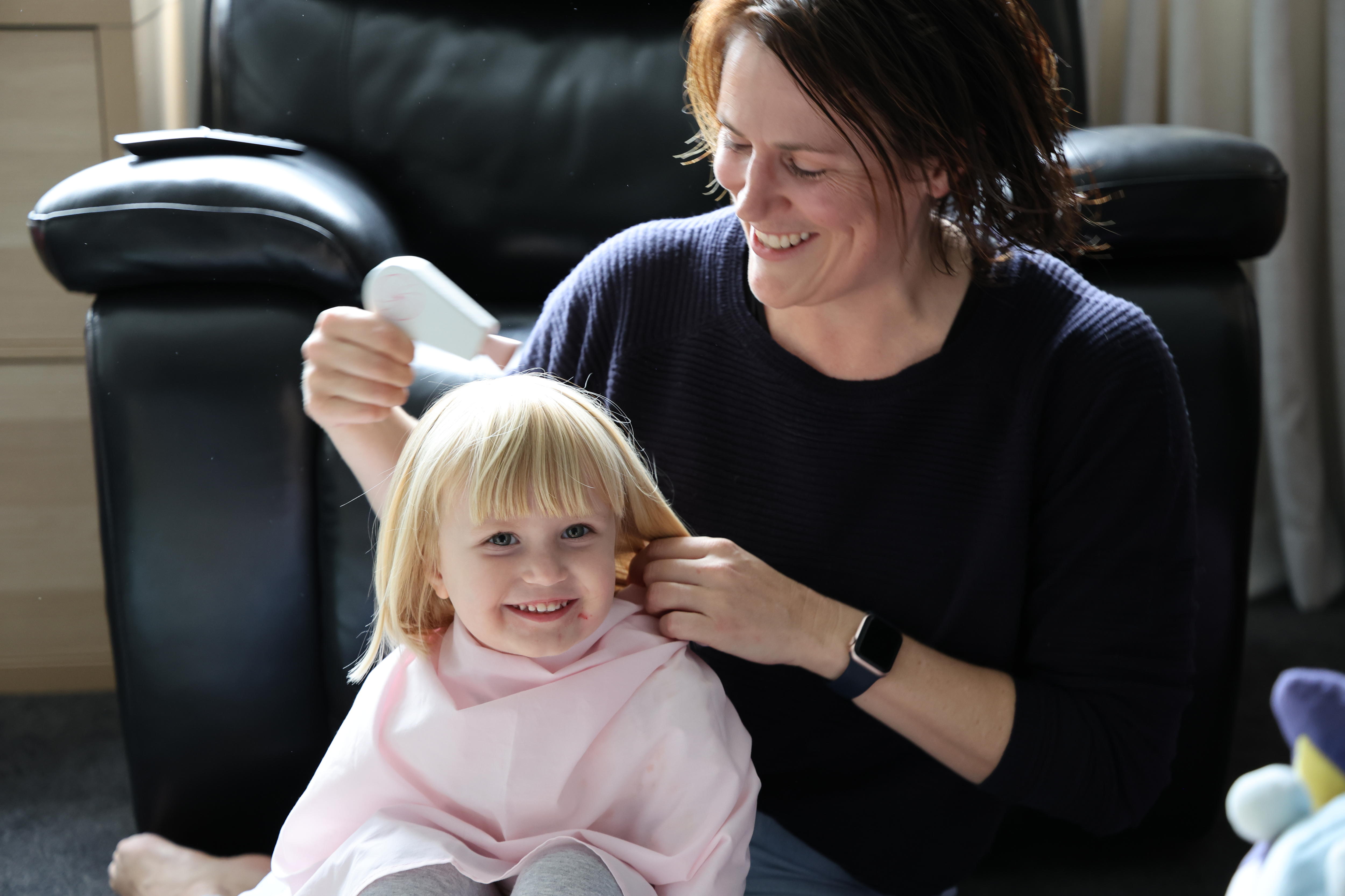 a little girl has her hair done by her mum.
