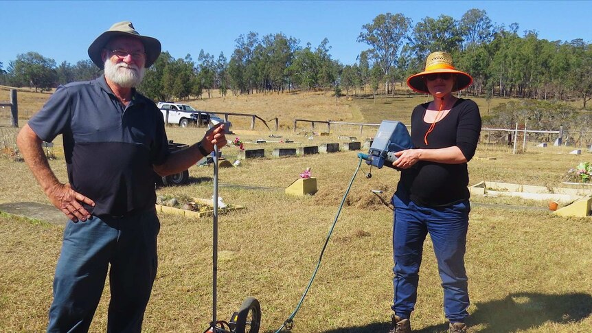 A man and a woman standing in a cemetery with technical equipment