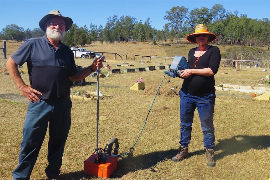 A man and a woman standing in a cemetery with technical equipment.