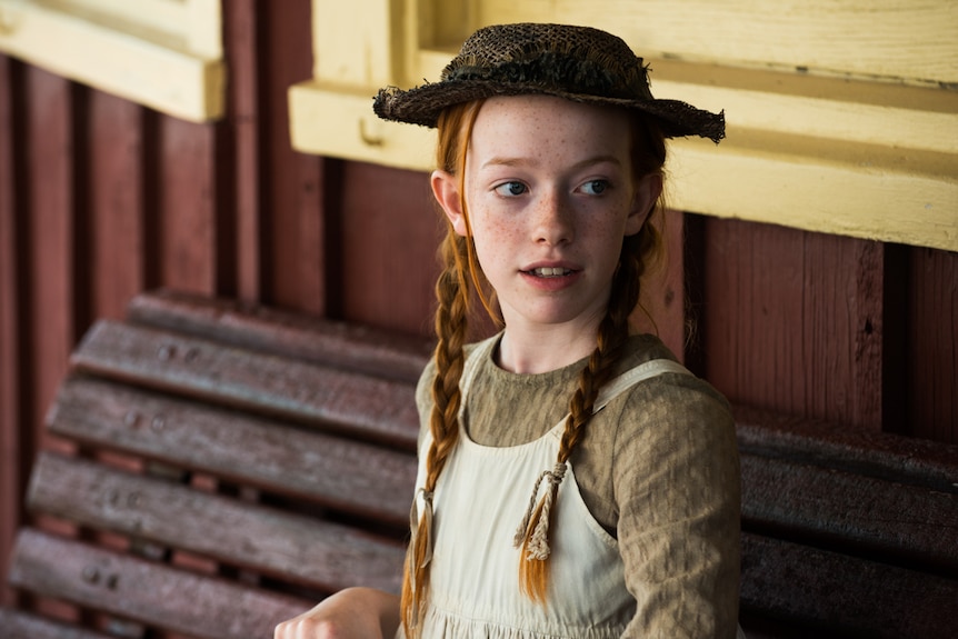 Girl with red hair sitting on bench in still from Anne of Green Gables in story about adaptations of children's classics.