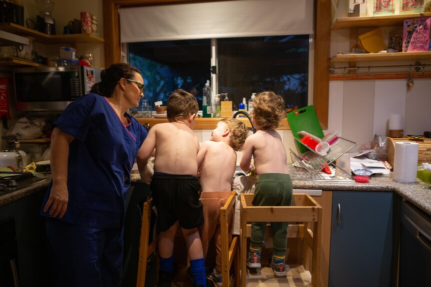 Bec stands with her three children at the kitchen sink.