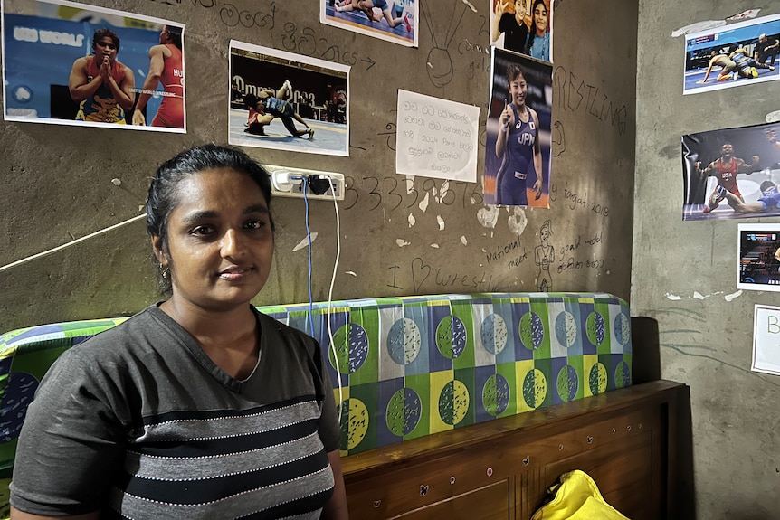 A Sri Lankan woman looks at the camera, there are pictures of wrestlers on the wall behind her.