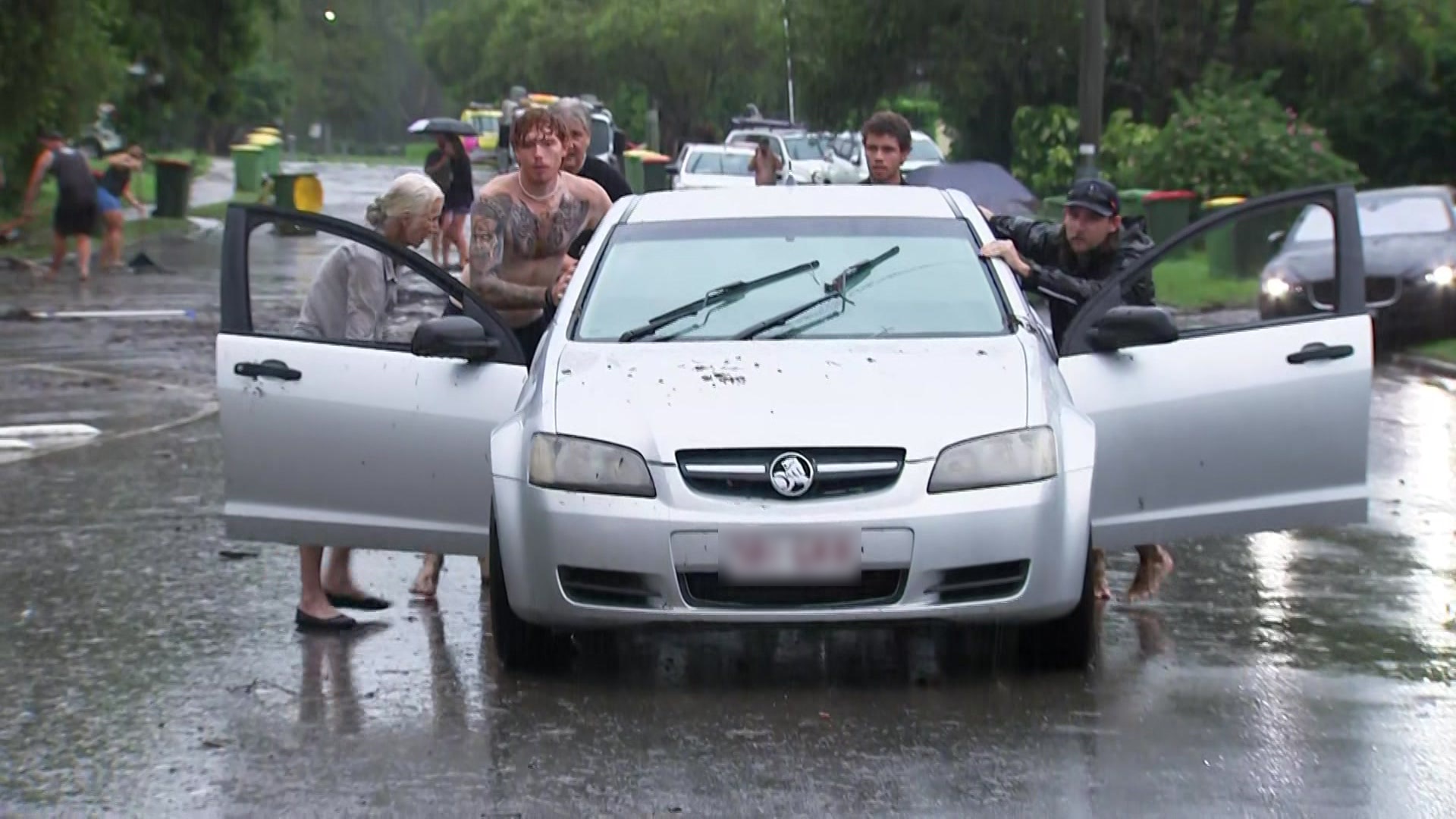 Three men push a car out of floodwater