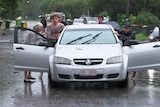 Three men push a car out of floodwater