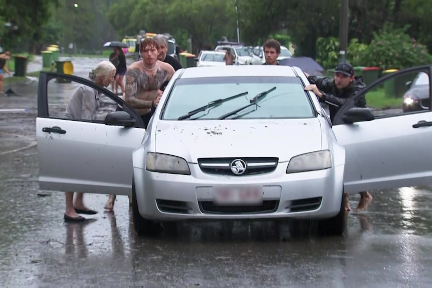 Three men push a car out of floodwater