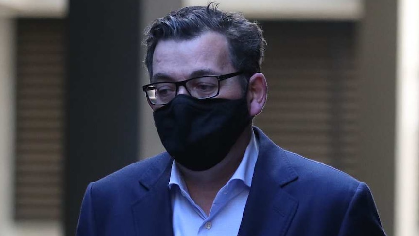 Daniel Andrews, wearing a black mask, looks down as he walks to a media briefing with a piece of paper in his hand.