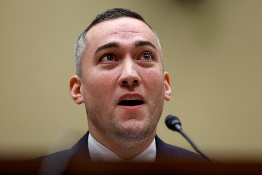 a man in a suit talking into a microphone looking serious