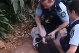 Two police officers restrain a teenager on the ground
