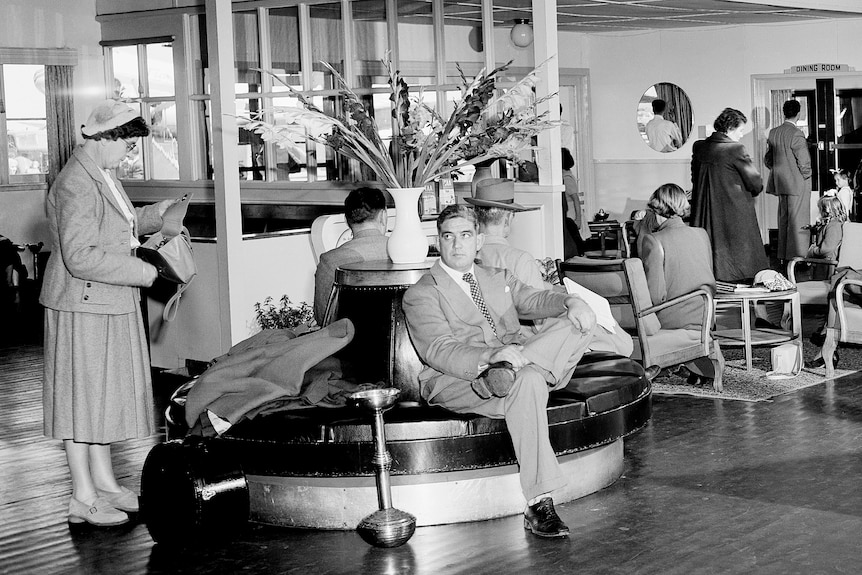 A black and white image of people waiting in a fancy old aiport.