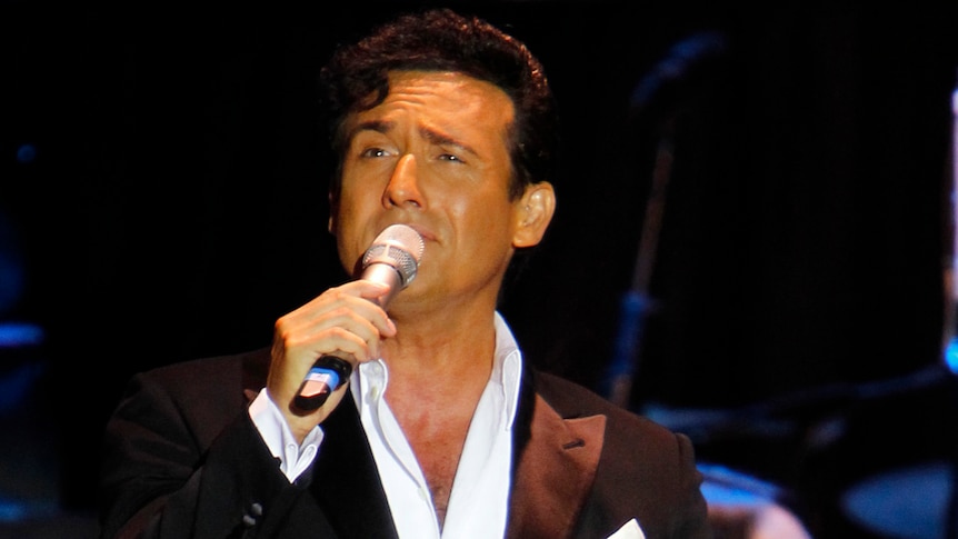 Carlos Marín sings into a hand-held microphone on stage.
