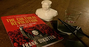 A book titled "The Cultural Revolution", a mini statue of Mao Zendong, a broken bowl and a glass cup.