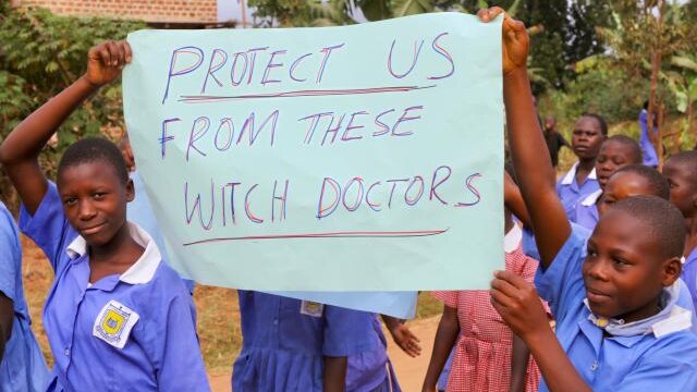 Ugandan children carrying a placard that says 'protect us from these witch doctors'.