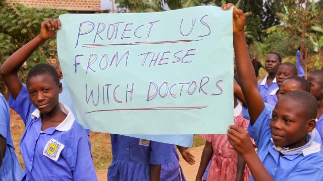 Ugandan children carrying a placard that says 'protect us from these witch doctors'.