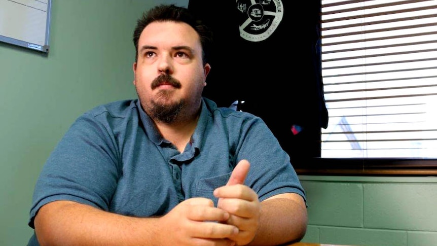 A man at a desk in a blue shirt with Transport Workers Union insignia behind him.