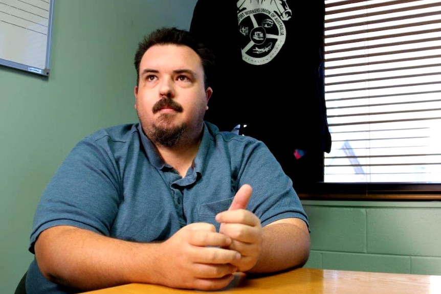 A man at a desk in a blue shirt with Transport Workers Union insignia behind him.