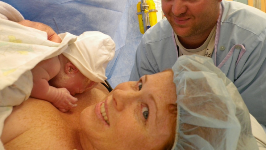 A mother holds her baby with her husband watching on.