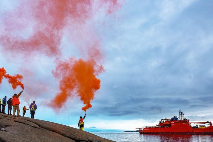 Expeditioners hold up flares with ship in the background.