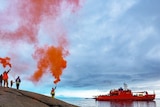 Expeditioners hold up flares with ship in the background.