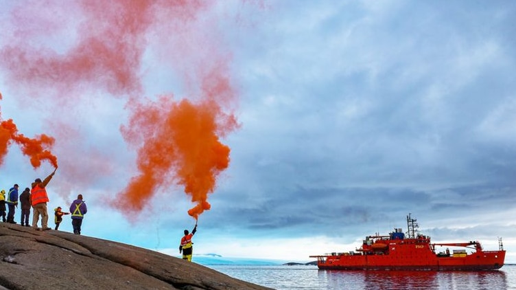 Expeditioners hold up flares with ship in the background.