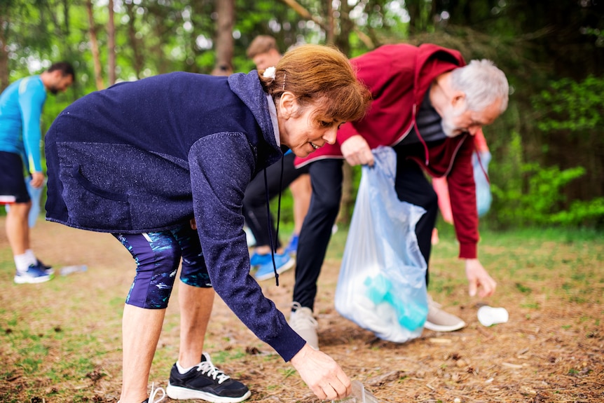 A woman bends down to pick up rubbish from a walking track.