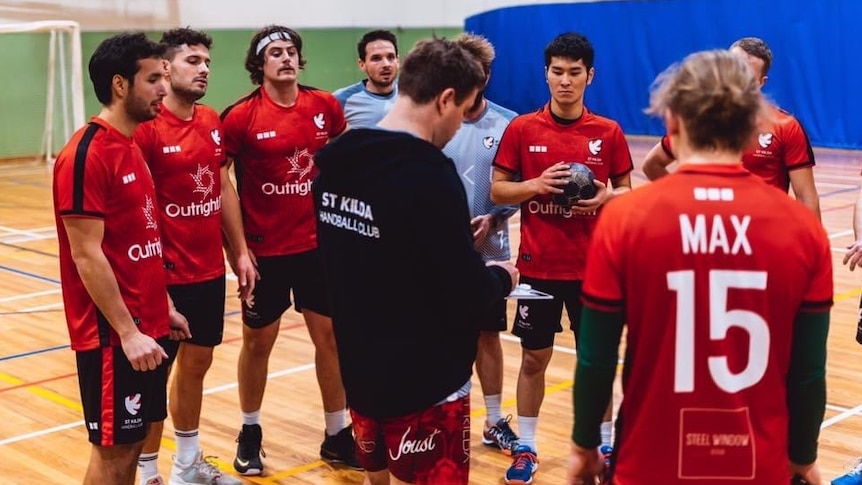 A coach and players stand around in a group in a gym at handball training.