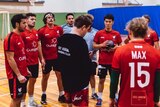 A coach and players stand around in a group in a gym at handball training.