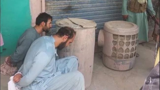Two detained Afghan officials sitting with their hands tied behind their backs.
