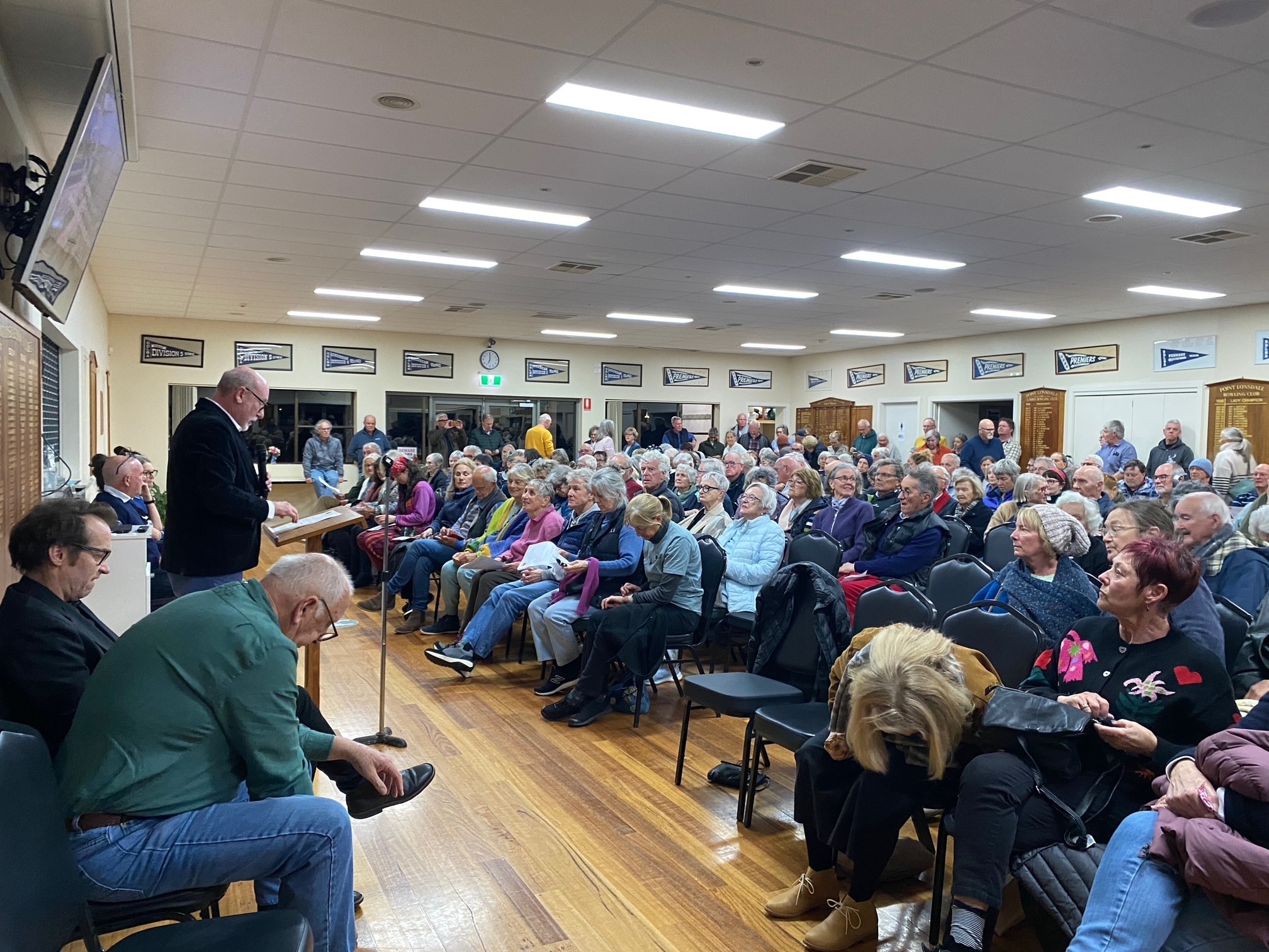 A group of more than 80 people mostly with grey hair sit in the Point Lonsdale bowls club at a community meeting. 