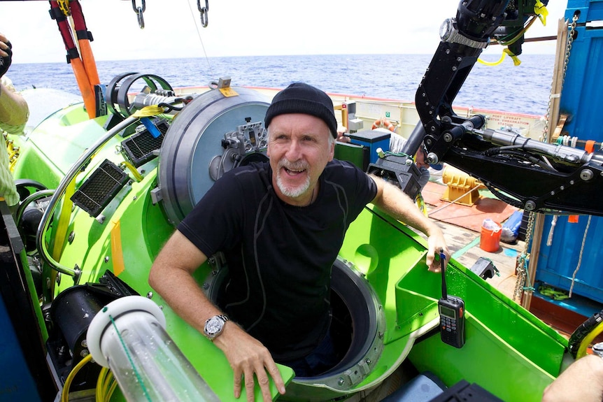 James Cameron gestures with his submarine behind him.