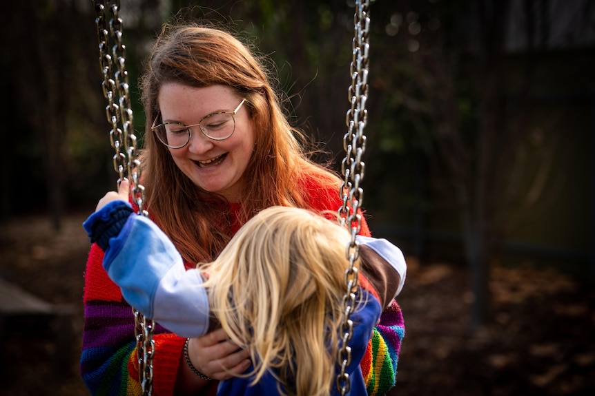 A mother pushes her toddler on a swing.