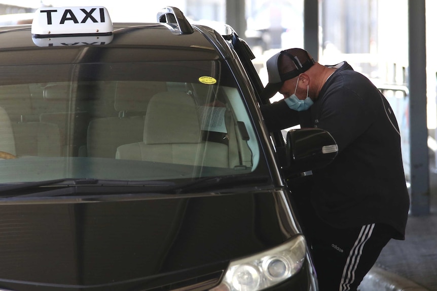 A man leans into a Perth Airport taxi wearing a surgical mask after a flight from Melbourne.