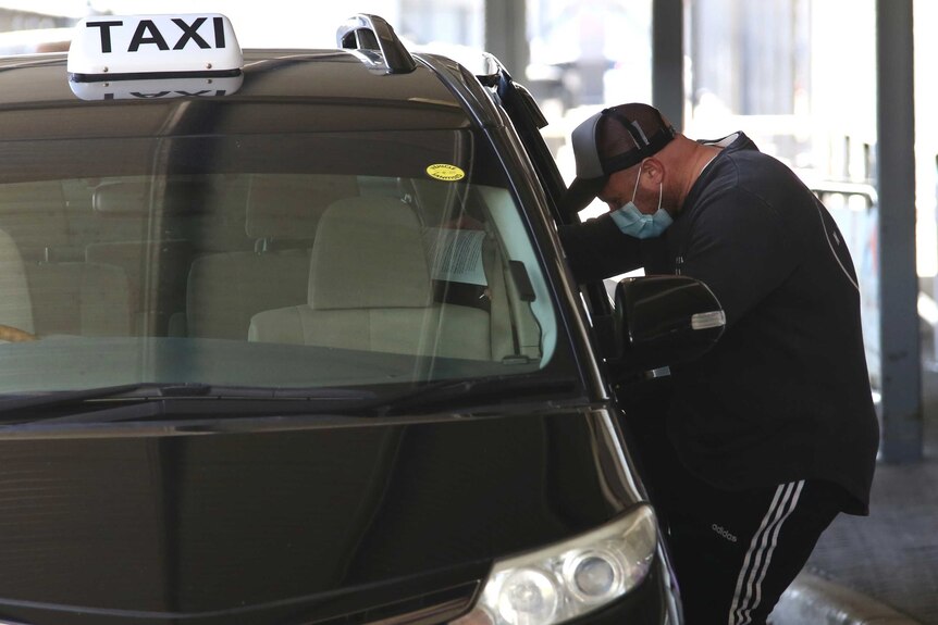 A man leans into a Perth Airport taxi wearing a surgical mask after a flight from Melbourne.