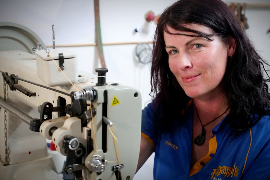 A woman with dark hair smiles. She is next to a leather sewing machine
