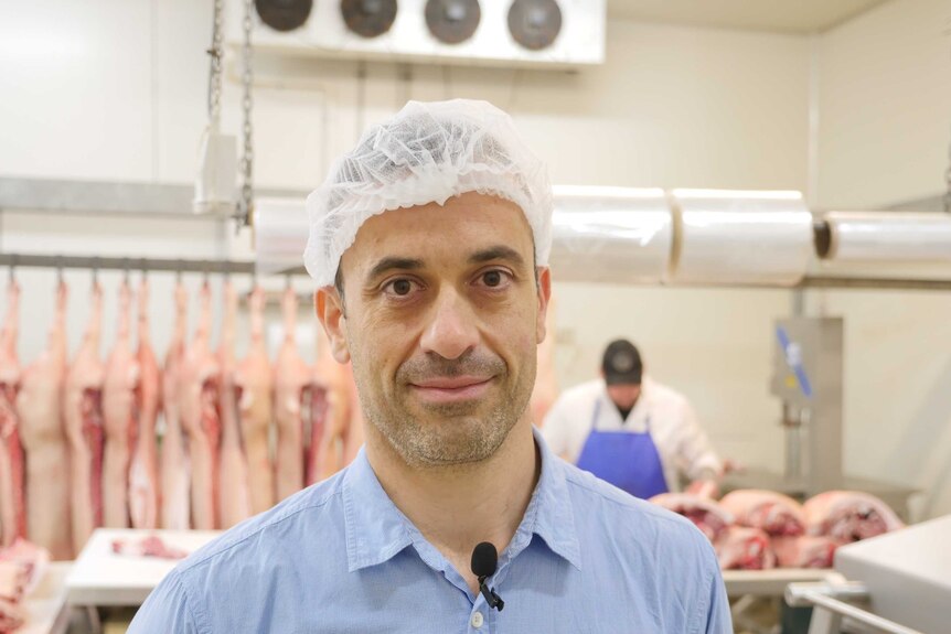 Robert Garreffa is standing in a meat room in Perth with pigs in the background
