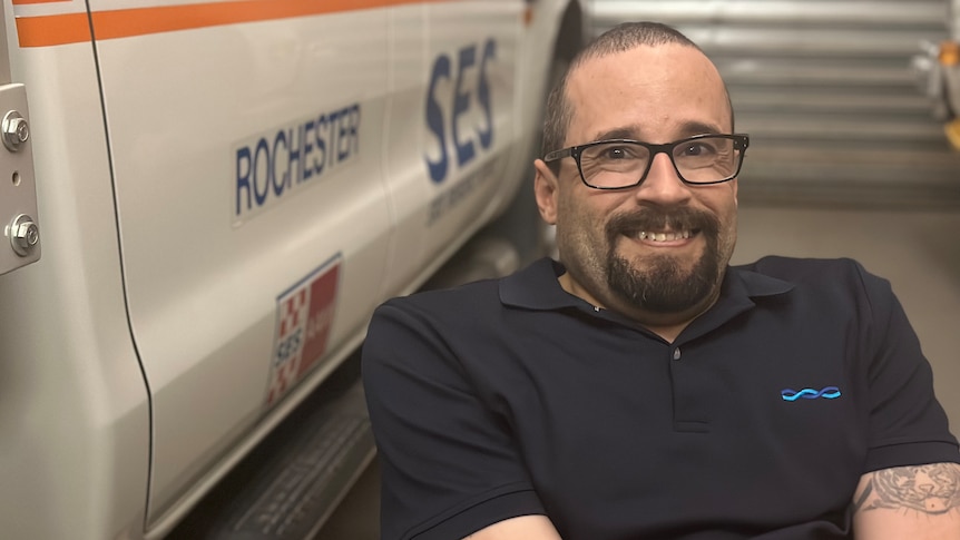 man with brown eyes, hair and a goatee and glasses with a big, happy, cheeky smile on his face