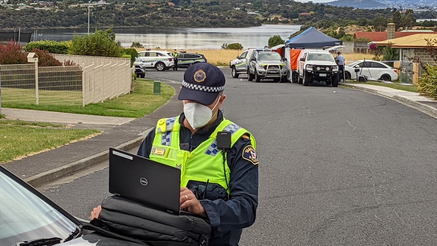 policeman looks at computer in front of forensics tent 