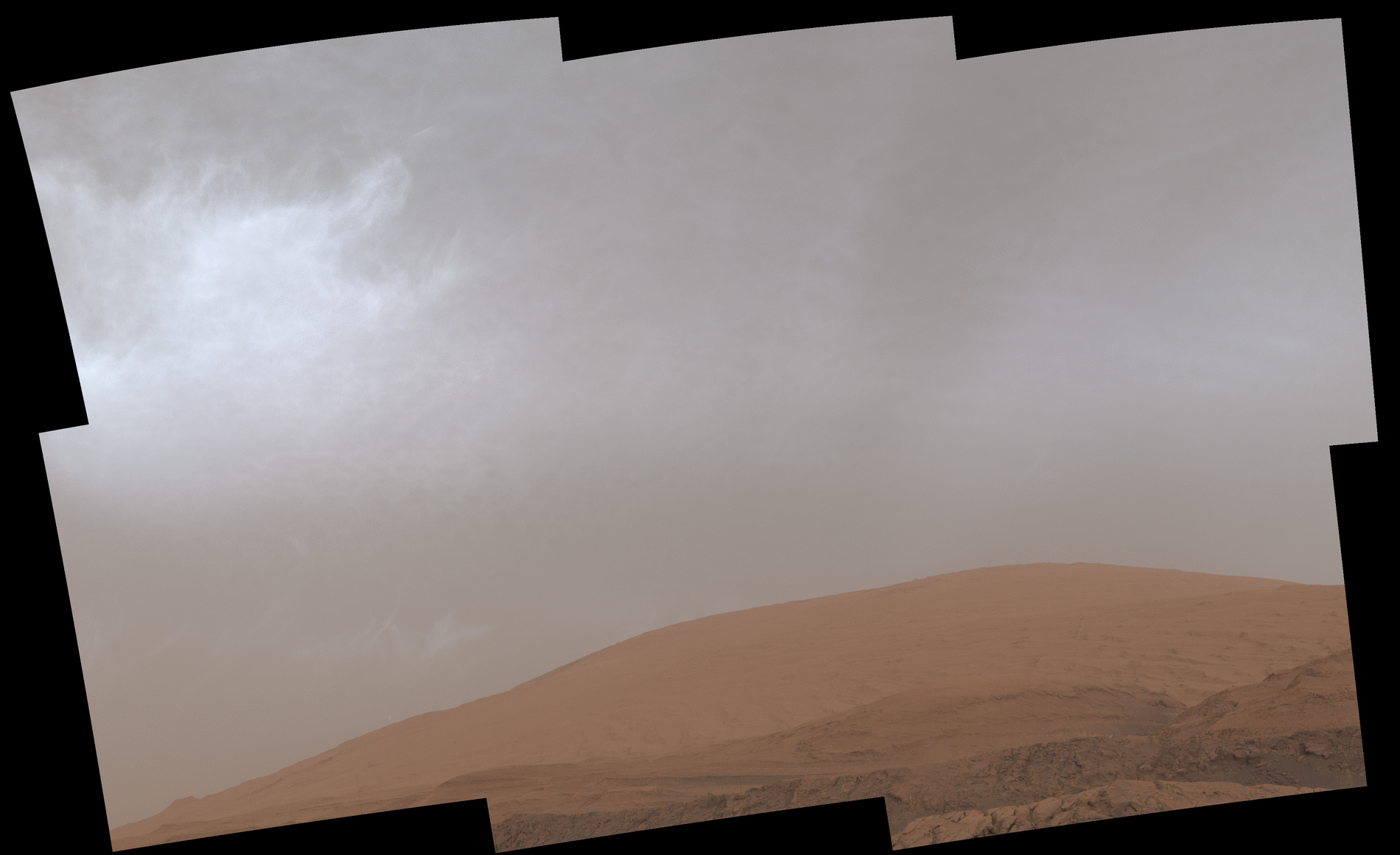 Grey clouds drift over a mountain on Mars
