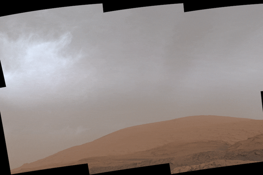 Grey clouds drift over a mountain on Mars