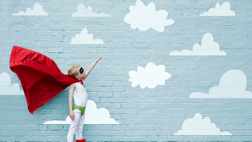 Boy in superhero costume points at painting of cloud on a brick wall