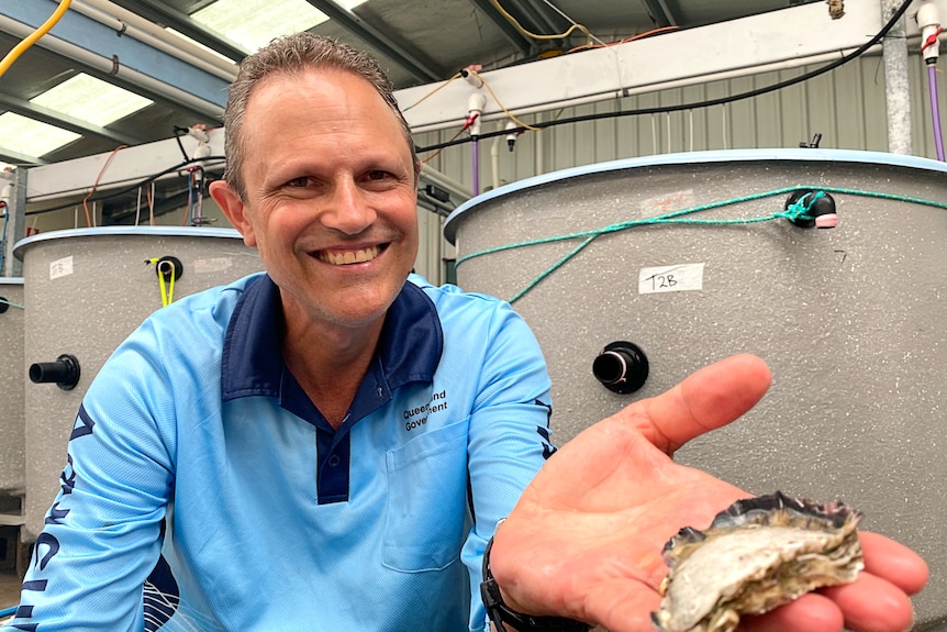 Man holding an oyster smiles at camera