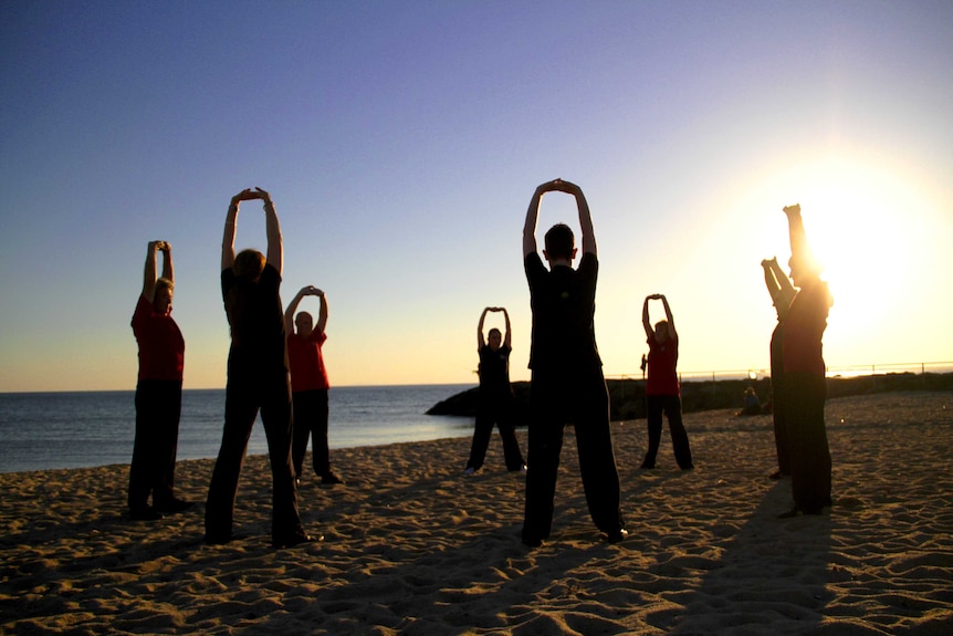 A group of people do Qigong on the beach.