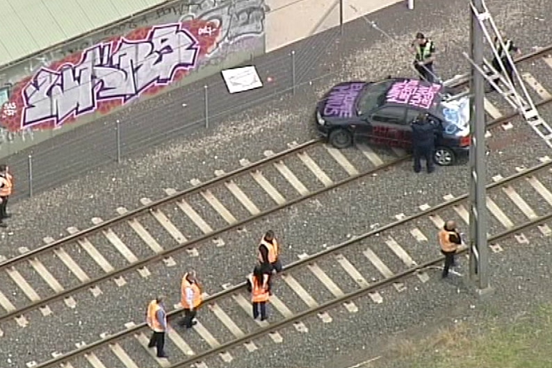 A car with the words 'Evacuate Manus' painted on it is parked across train tracks.