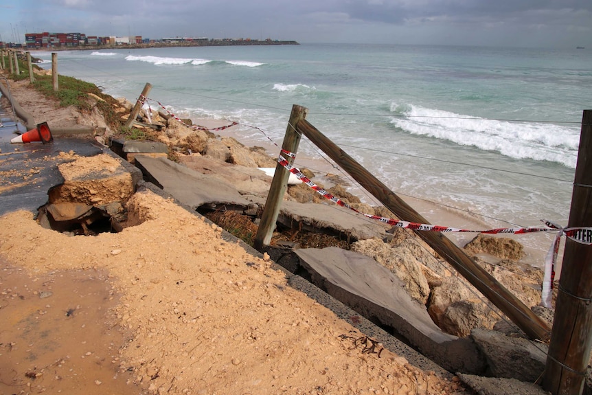 Eroded bitumen, concrete and fence with warning tape at Port Beach, Fremantle.