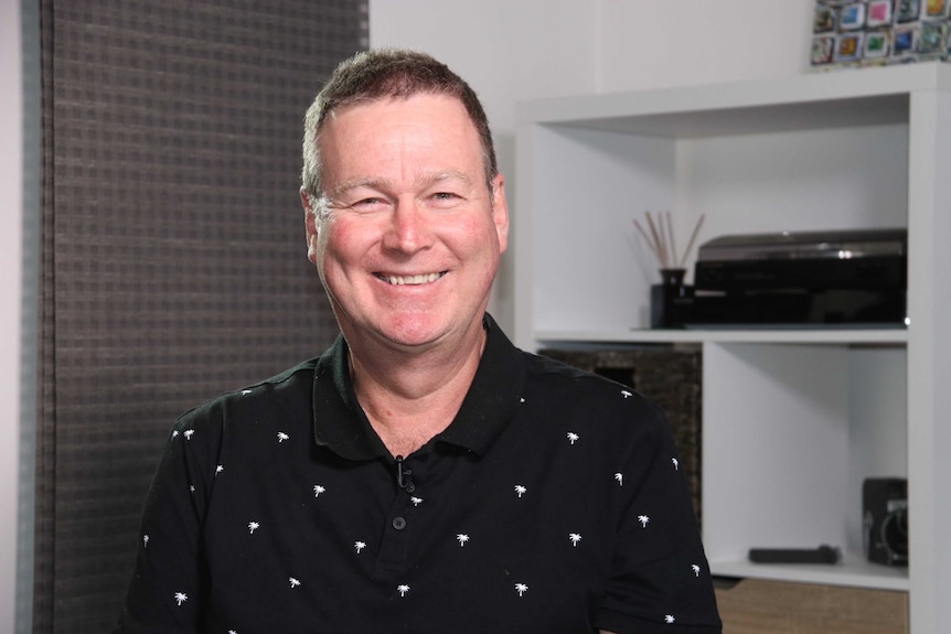 A middle-aged man in a black polo shirt smiles at the camera