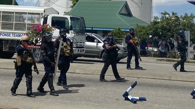 Six armed police officers walk through the streets of Honiara.
